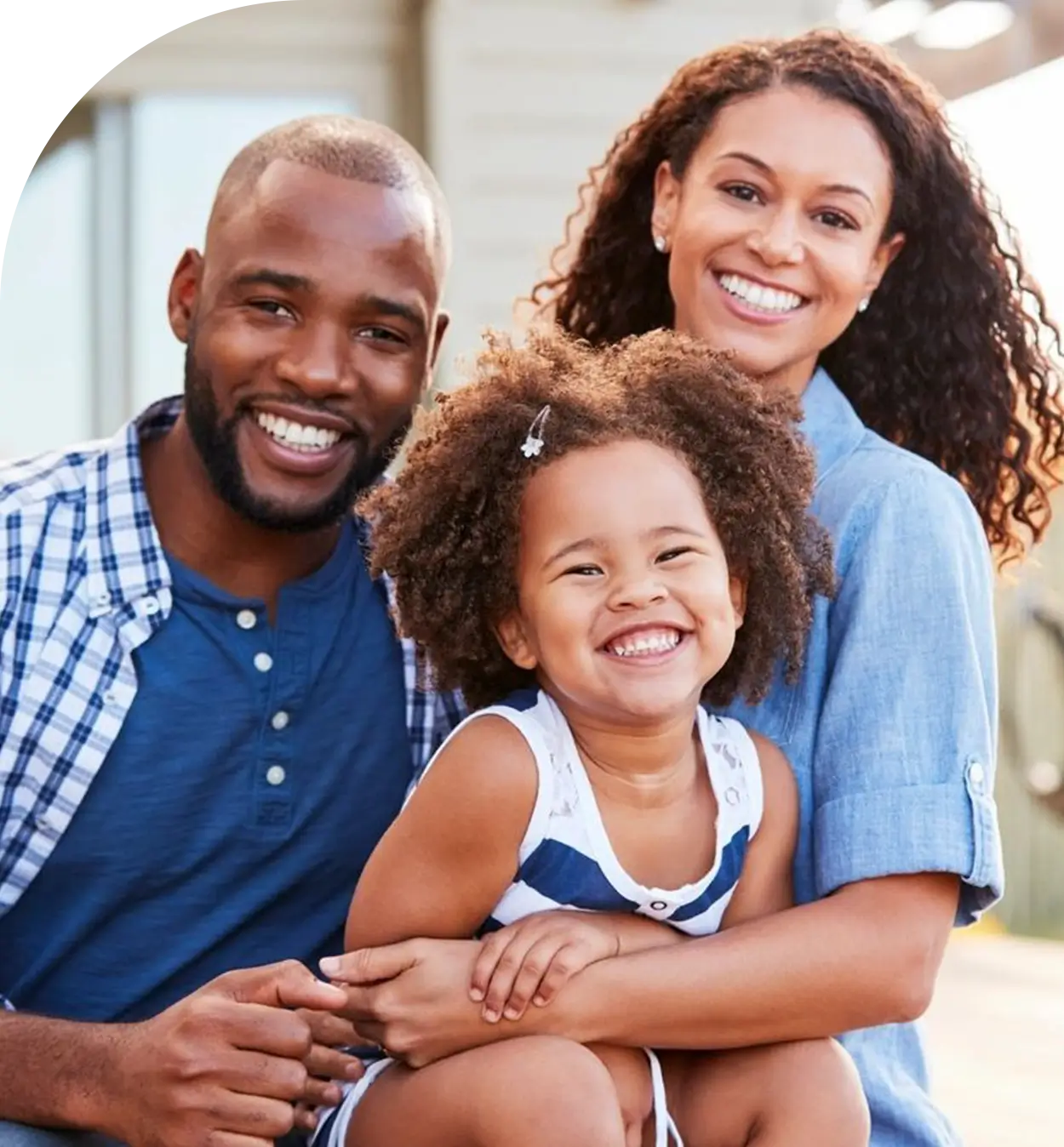 A smiling family of three, consisting of two adults and a child, poses together outdoors.